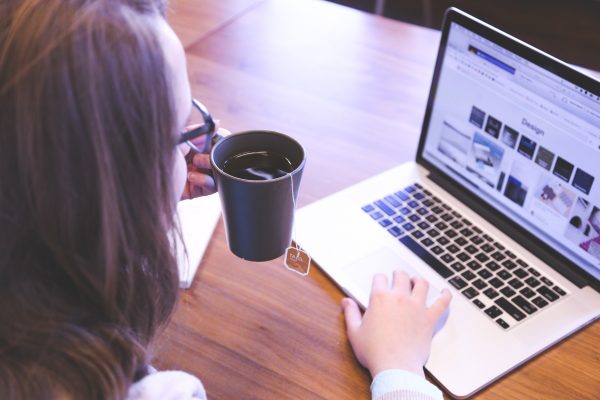 Woman sitting at a table drinking coffee in front of her laptop, working on her web presence