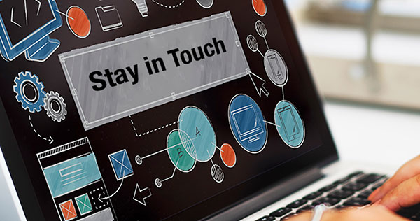 Fingers on keyboard of laptop computer with the words "Stay in Touch" on the screen